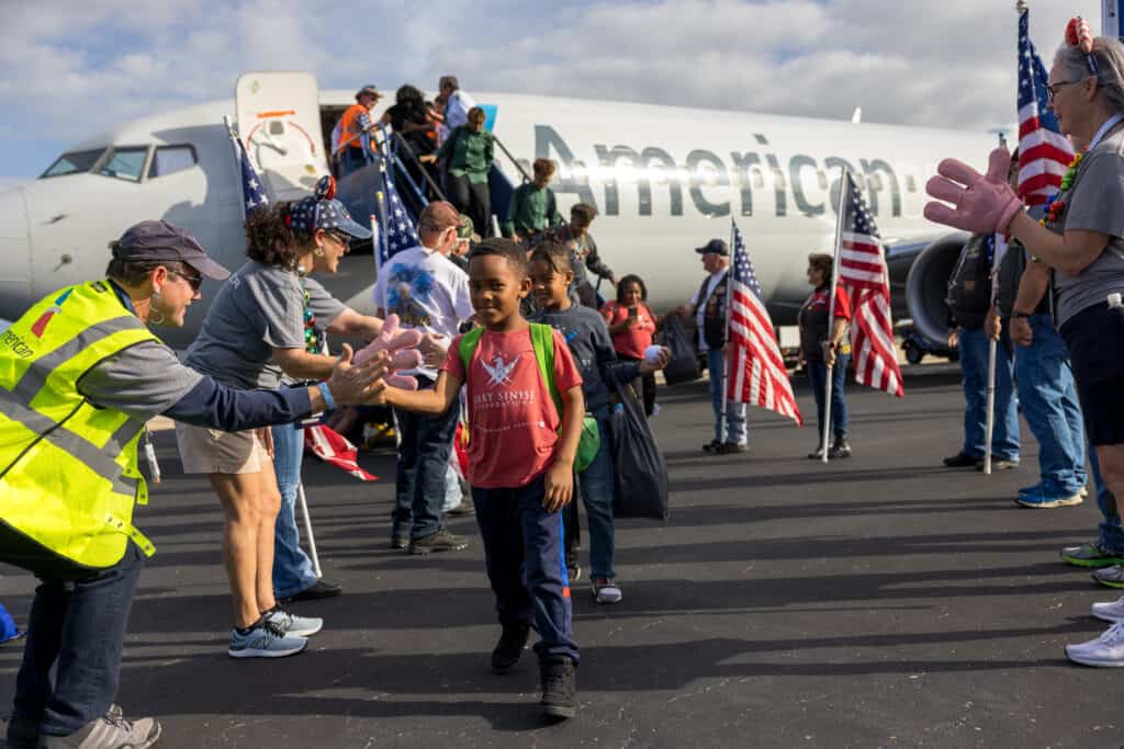people exiting a plane to a warm welcome with American flags all around for the Gary Sinise Foundation
