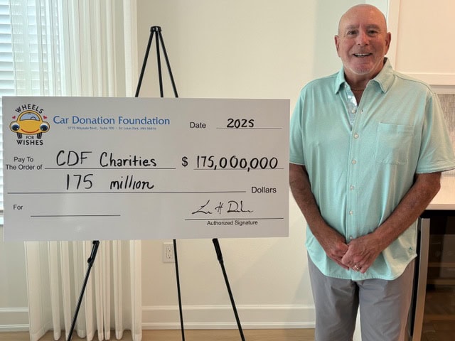 Car Donation Foundation Executive Director, Loren Dorshow, stands next to big check addressed to CDF charities for $175 million